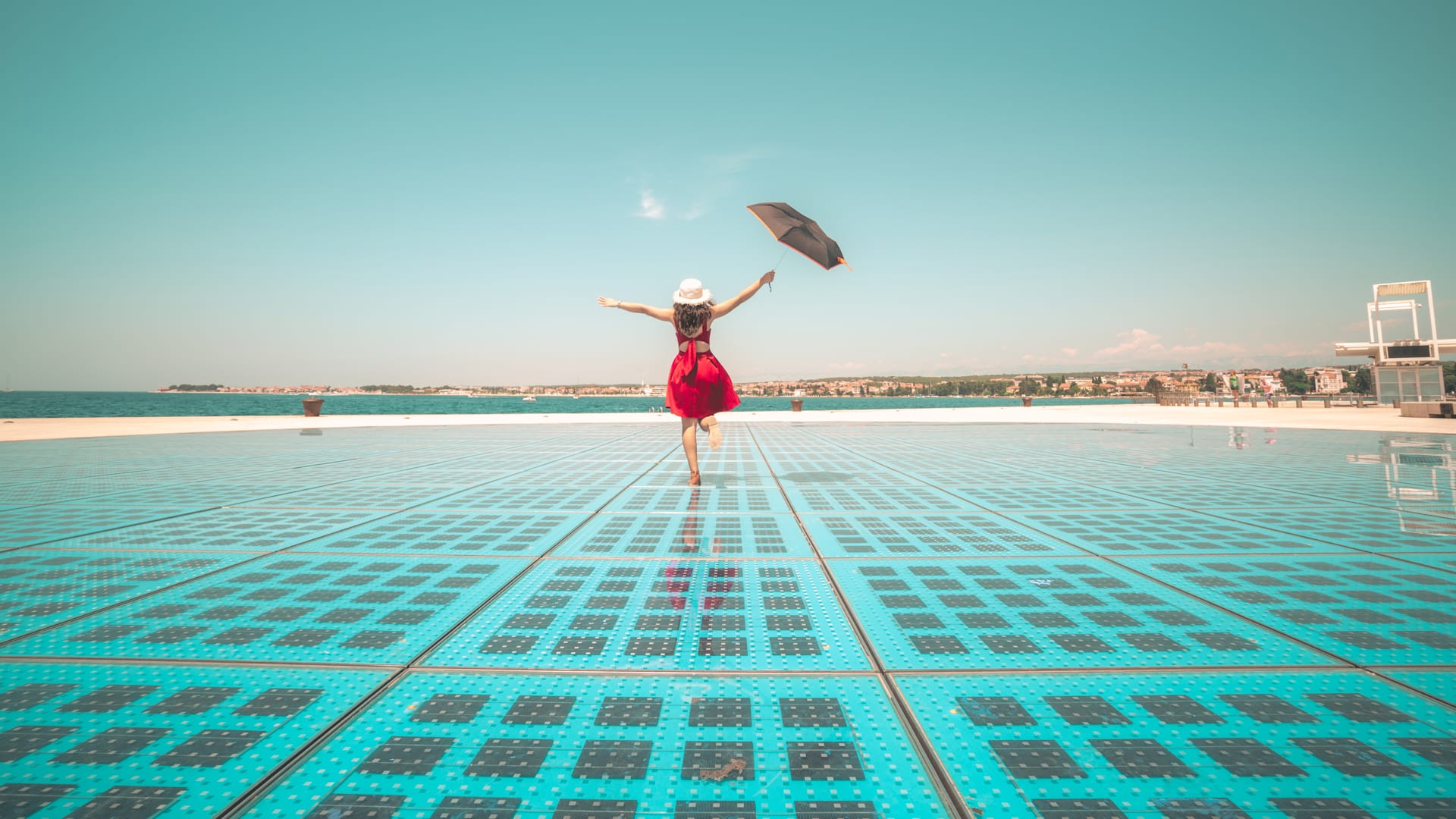 Woman in red dress flies kite on sunny day at Zadar's Sea Organ.