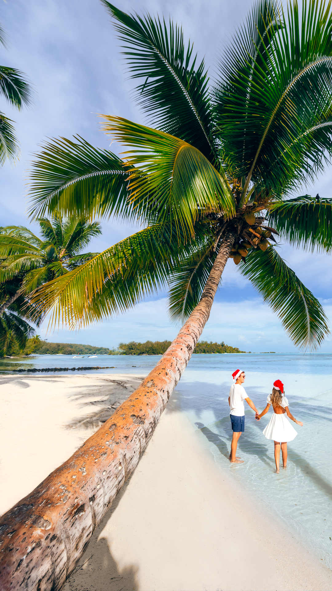 Two Windstar Cruise passengers in Santa Claus hats walking along a beach shore